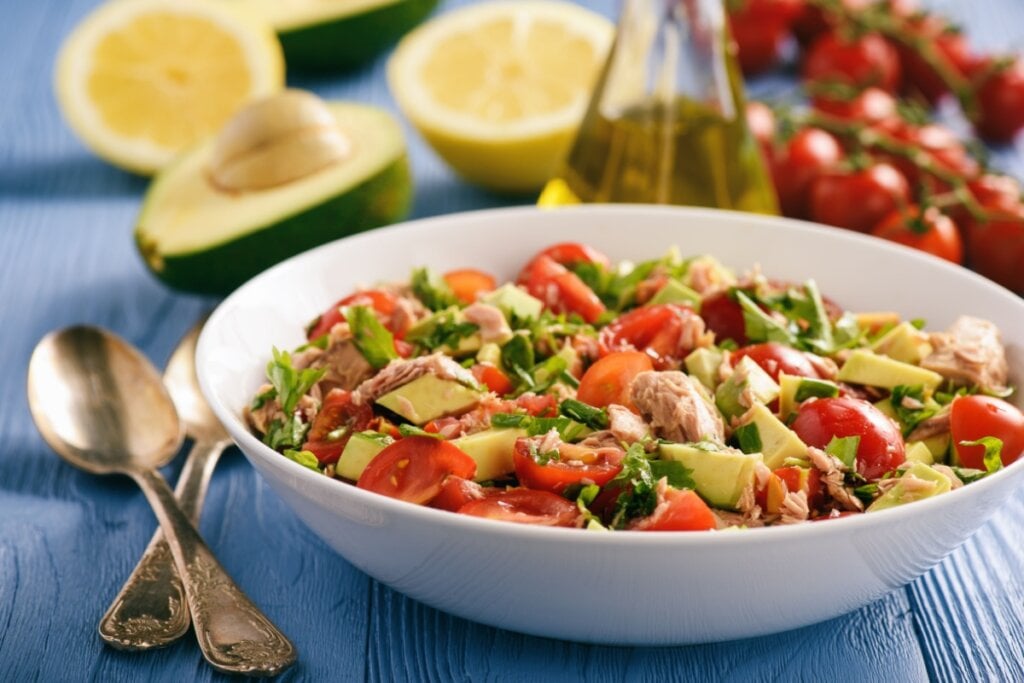 Salada de atum com abacate servido em prato fundo branco em cima de mesa de madeira azul