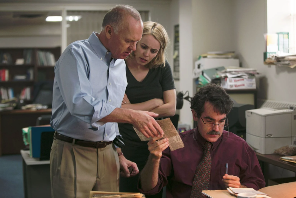 Três jornalistas analisando recortes de jornal em uma redação, representando uma das investigações no filme Spotlight – Segredos Revelados