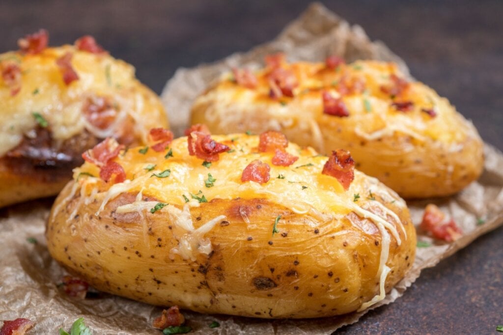 Batata recheada com bacon e requeijão servido em guardanapo em cima de mesa de madeira