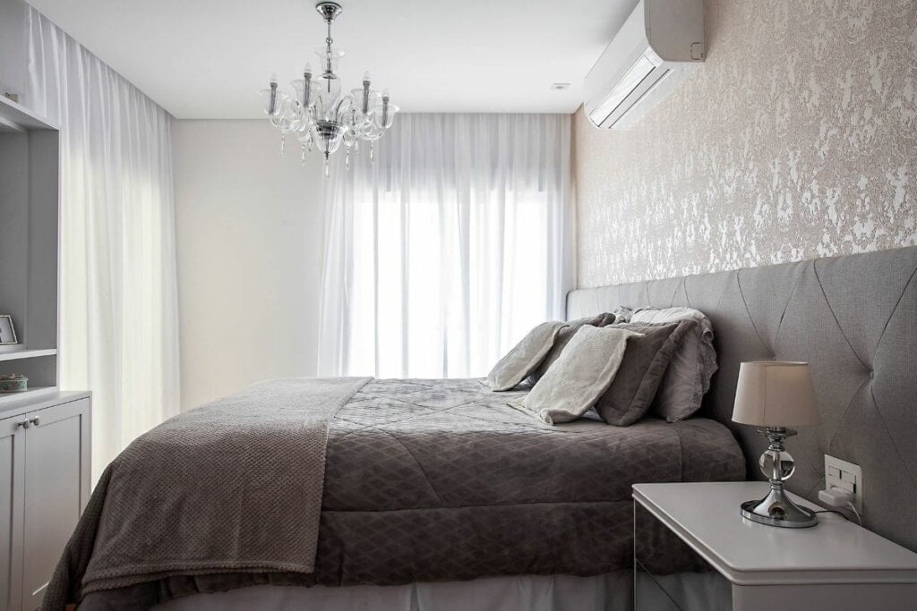 Cabeceira com integração estofada marrom em um quarto com papel de parede marrom, lustre e cortinas brancas 