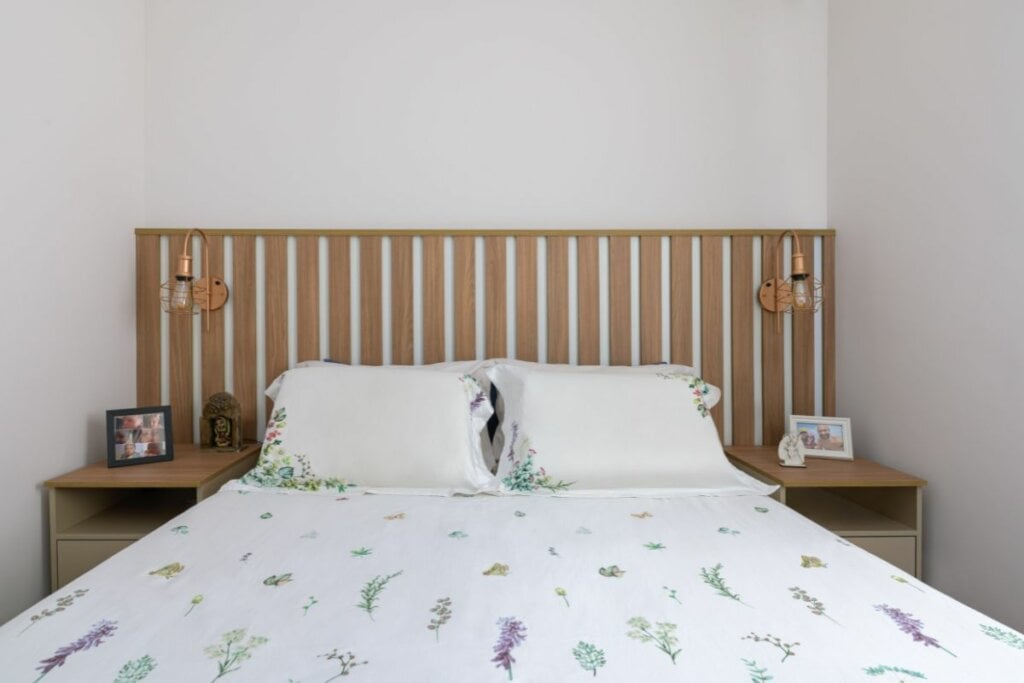 Cabeceira com madeira ripada atrás de uma cama com lençol branco 