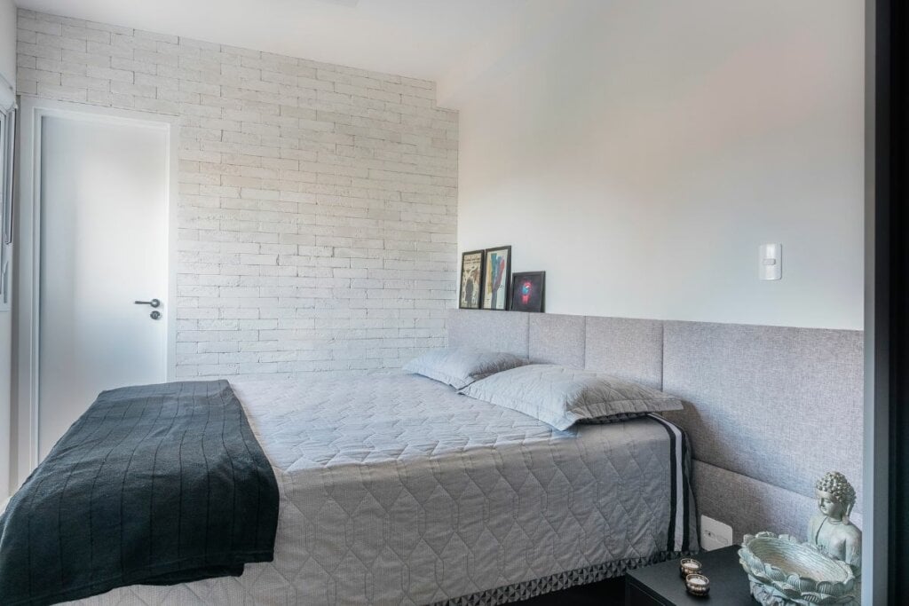 Cabeceira com estofado cinza atrás de uma cama com lençol cinza e manta verde 