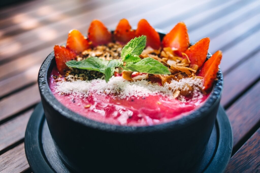 Recipiente preto com creme de pitaya, morangos, coco ralado e chips de coco