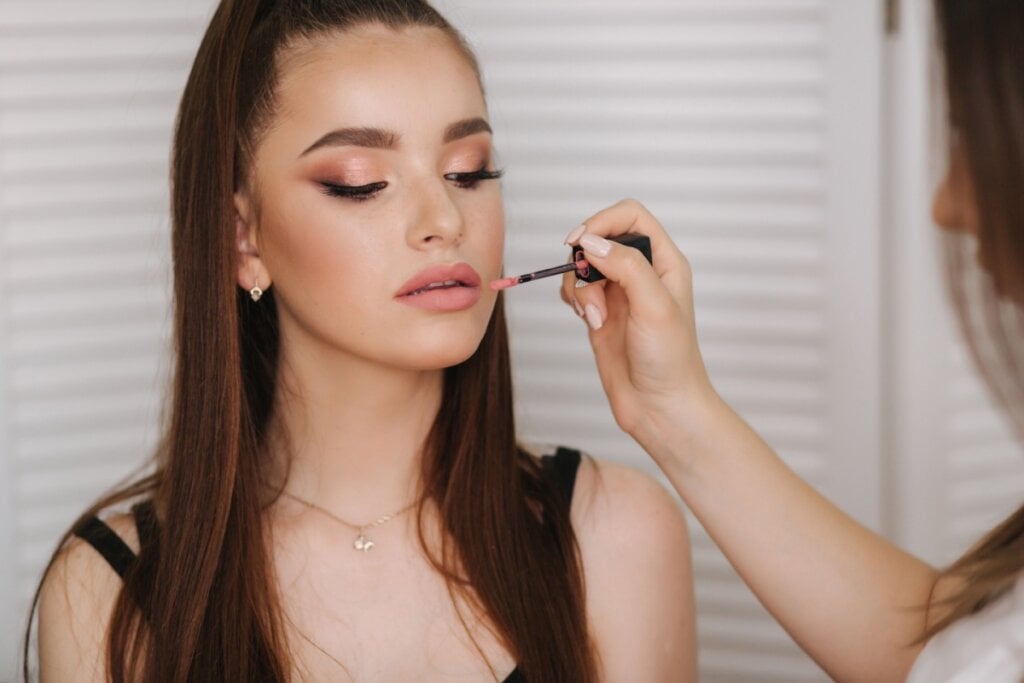 Mulher com olhos fechados e uma mão passando batom em sua boca 