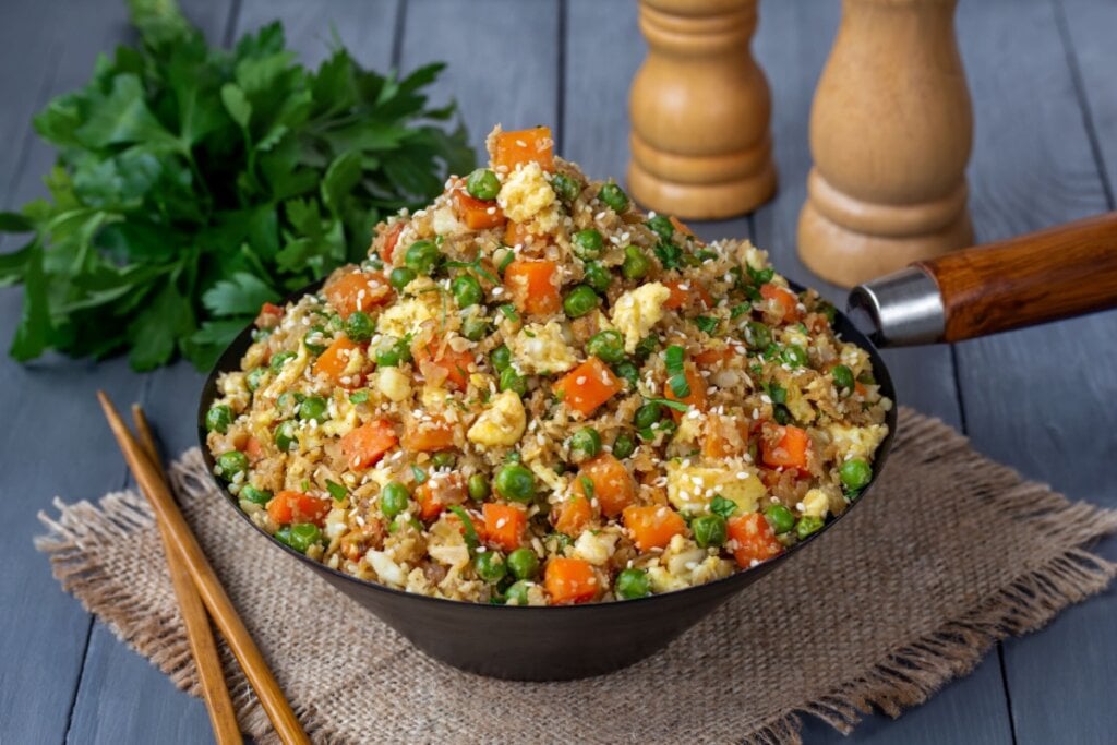 Arroz de couve-flor com ovo, cenoura, ervilha e temperos servido em frigideira em cima de mesa de madeira