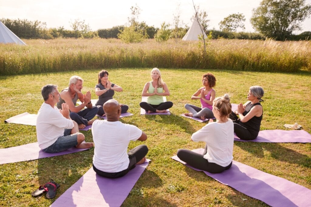 Pessoas reunidas em uma roda, ao ar-livre, fazendo meditação 