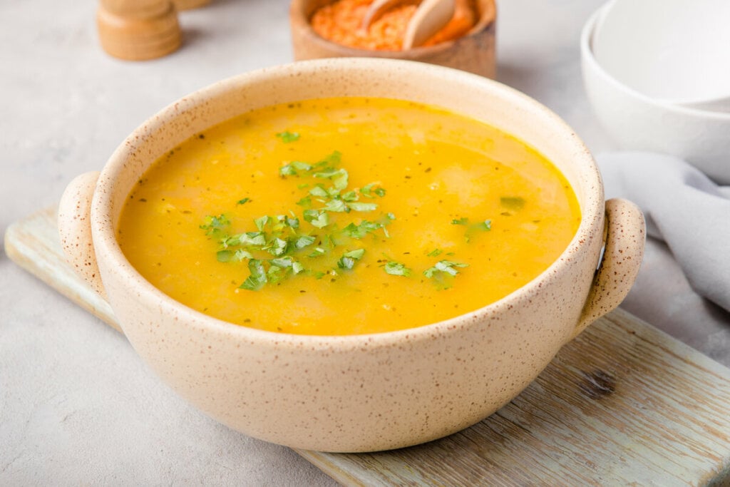 Recipiente bege com sopa de cenoura polvilhada com coentro picado