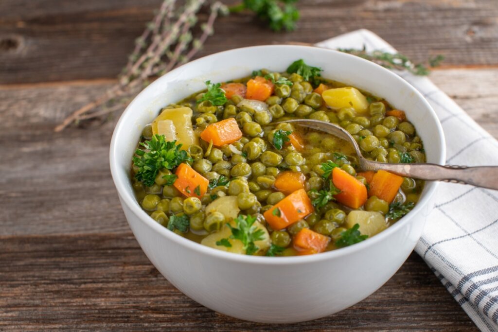 Sopa de ervilha com legumes servido em tigela de porcelana branca em cima de mesa de madeira