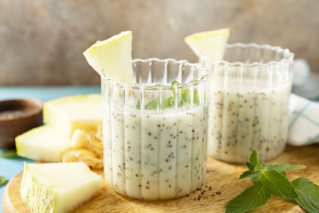 Dois copos com vitamina de melão com chia decorado com rodelas de melão e folhas de hortelã