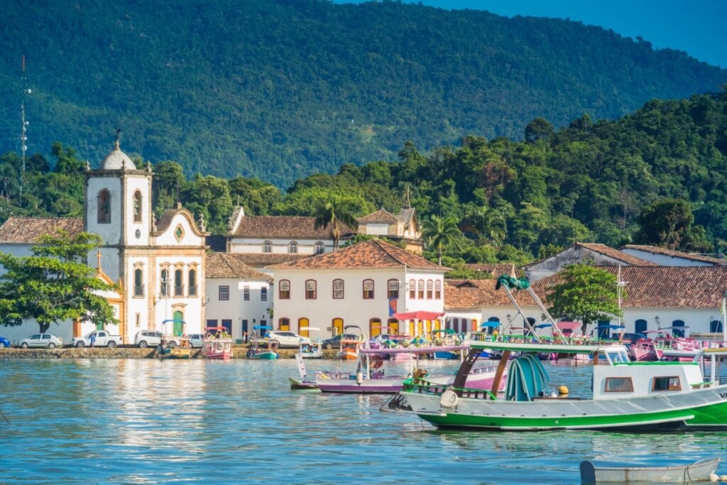 Vista de Paraty, RJ, com barcos no mar, igrejas históricas e montanhas ao fundo