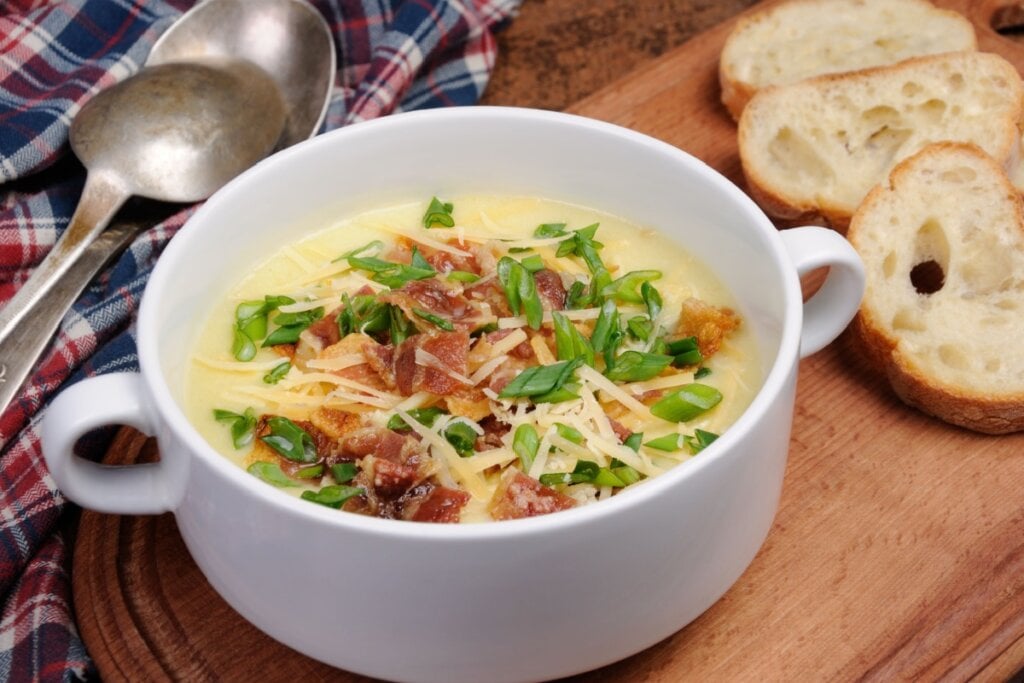 pote branco de porcelana com sopa de mandioca com bacon, queijo e cebolinha em cima