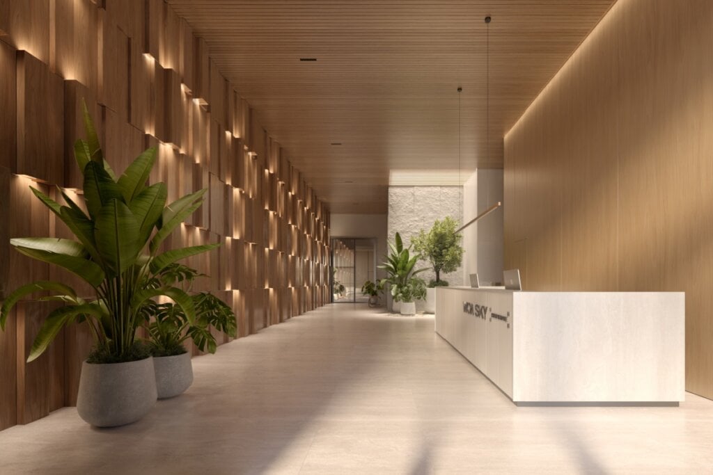 Recepção corporativa com balcão branco minimalista à direita, parede lateral revestida com painéis de madeira em relevo e iluminação embutida, teto ripado e vasos grandes com plantas tropicais