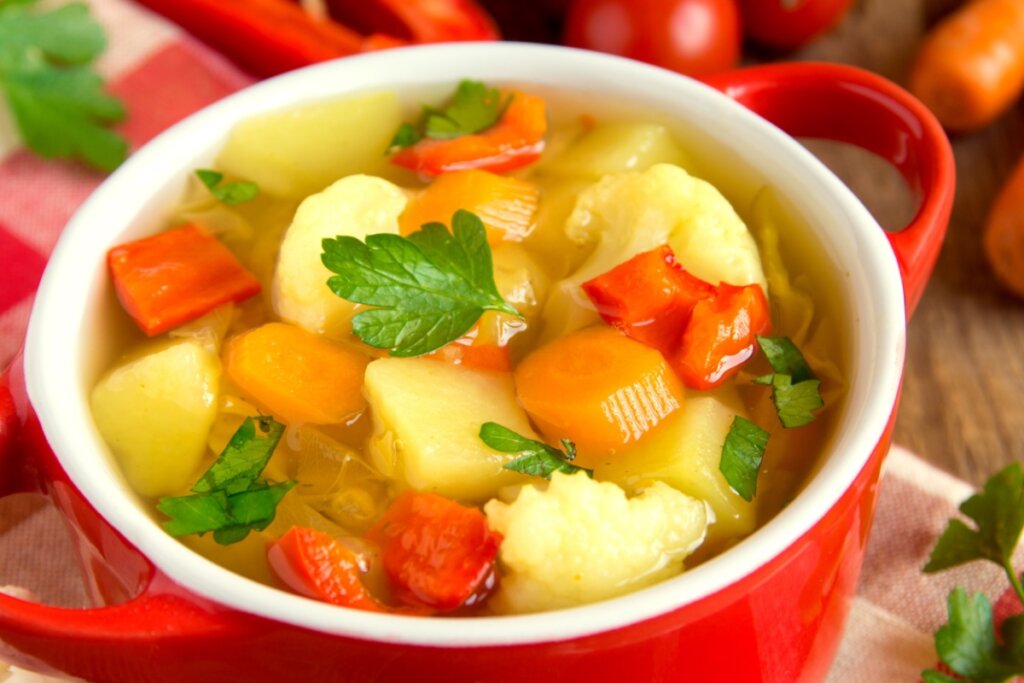 Panela vermelha com sopa de cenoura com batata, pimentão vermelho e couve-flor