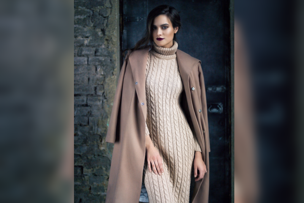 Mulher de vestido longo de tricô e casaco sobre os ombros em ambiente com tijolos
