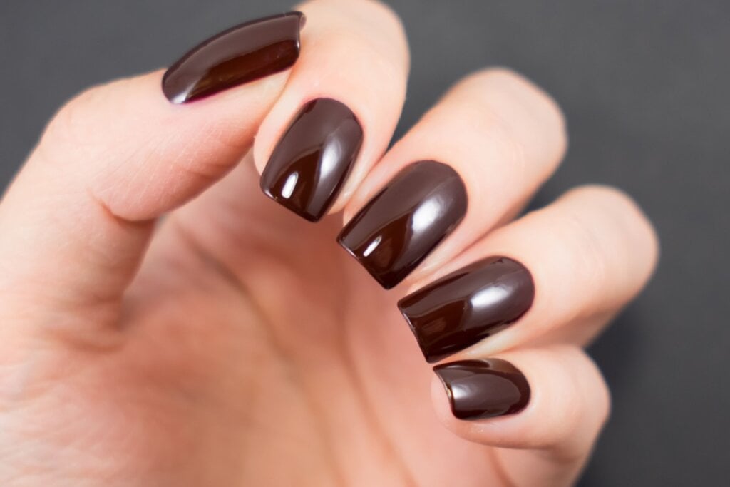 mão com unhas femininas em tom de marrom-escuro