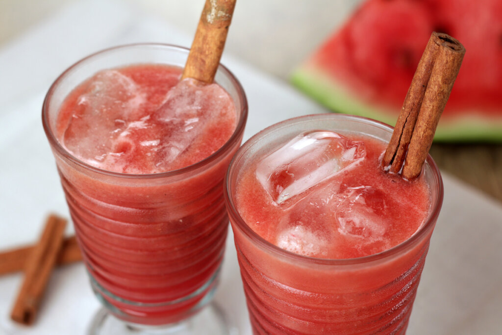 Suco de melancia em dois copos com pedras de gelo e canela em pau