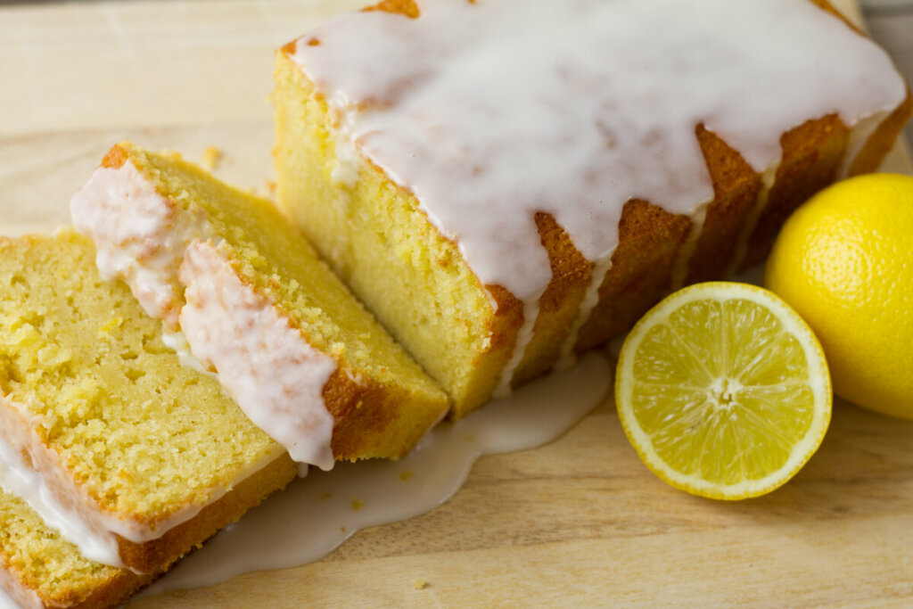 Bolo de limão com calda com dois pedaços cortados em cima de uma mesa de madeira com rodelas de limão