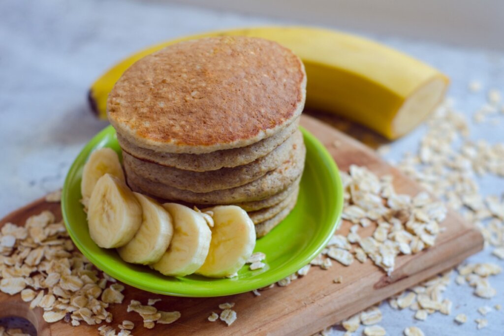 Panquecas de aveia e banana e whey servidas empilhadas em prato de cerâmica verde com rodelas de banana