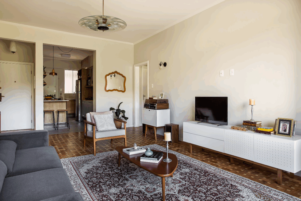 Sala de estar com móvel em branco com TV e cadeira de madeira com estofado branco e sofá preto e tapete estampado no chão