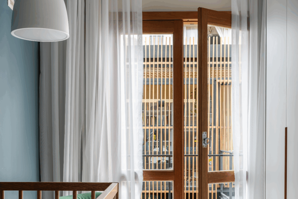 Porta de madeira com vidro em sacada de quarto com cortina branca