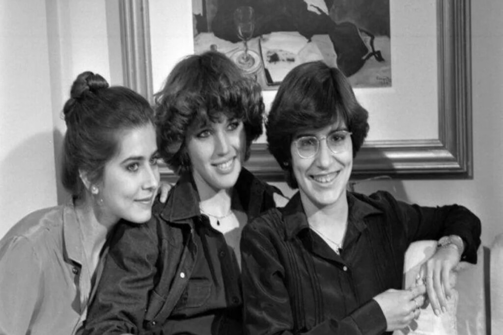 imagem em preto e branco de três mulheres, uma ao lado da outra, sorrindo