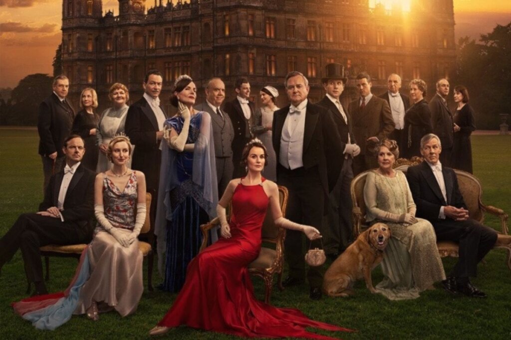 Capa do filme "Downton Abbey – O Grande Final" com os personagens vestindo roupa de gala e reunidos em frente a um castelo ao pôr do sol 