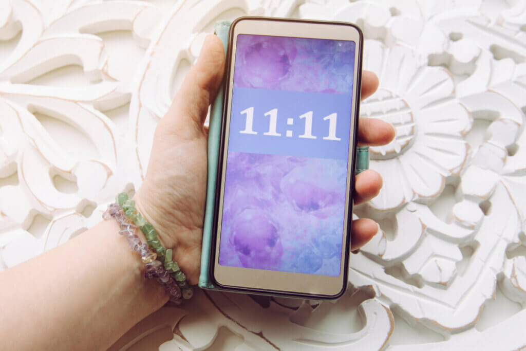 mão segurando celular mostrando 11:11 na tela com fundo roxo
