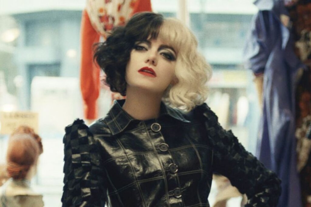 Emma Stone como Cruella, usando roupa preta, cabelo bicolor preto e branco e batom vermelho