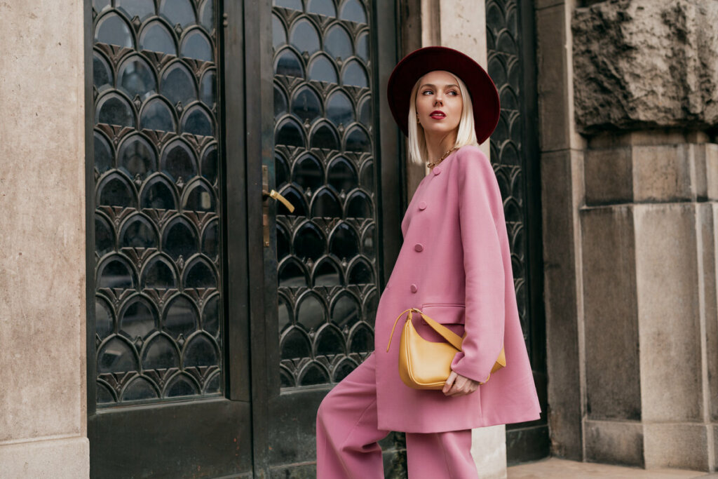 Mulher com calça, blazer rosa e chapéu olhando para o lado