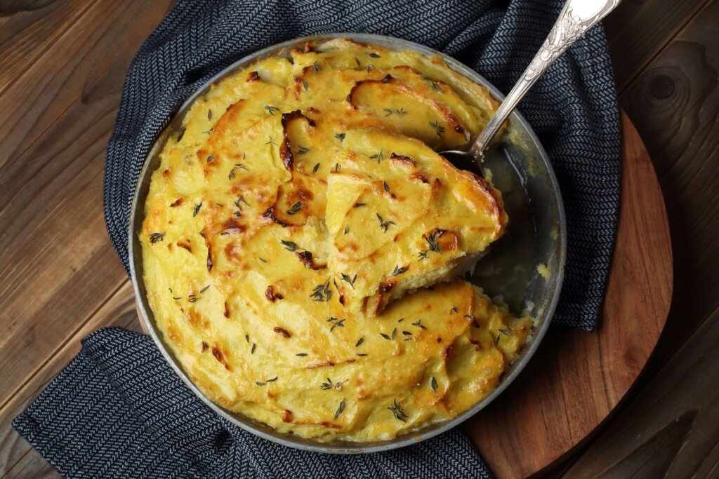 Gratinado de peixe com batatas em forma e colher com um pedaço do prato