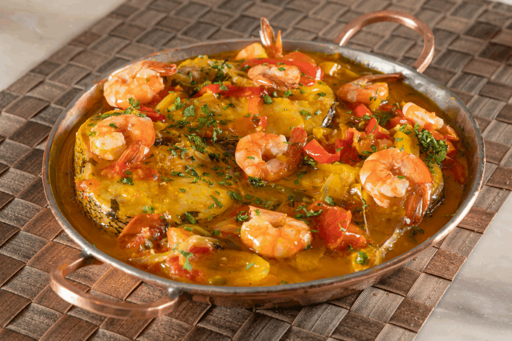 Moqueca de peixe servida em panela de ferro em cima de mesa de madeira