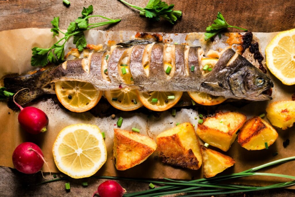 Peixe recheado com limão e batatas assadas servido em cima de mesa de madeira