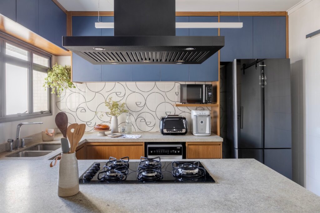 Cozinha com cooktop na ilha, armários superiores azuis e parede com revestimento de linhas curvas