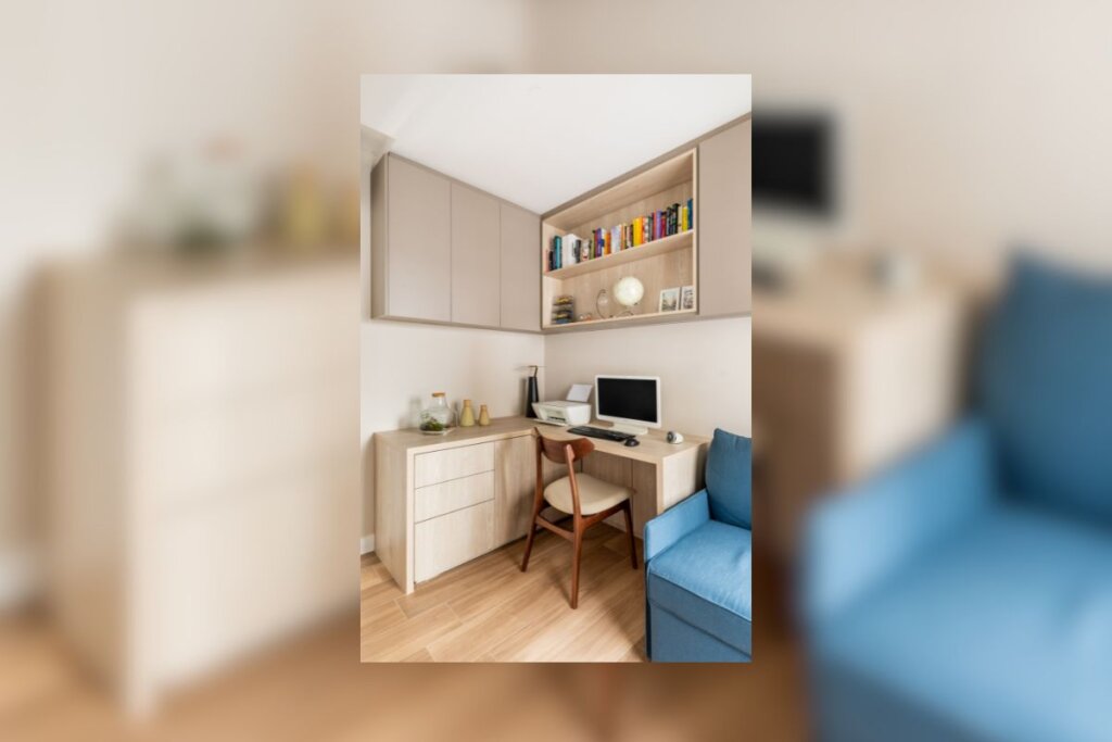 Quarto com armários bege-claro com livros, abaixo dele, uma mesa branca com computador e, ao lado, um sofá azul 
