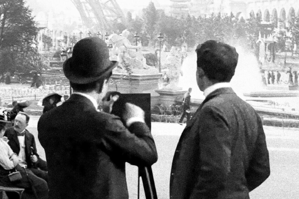 Foto em preto e branco, com dois homens virados de costas, fotografando árvores em um parque, no filme Lumière! A Aventura Contínua