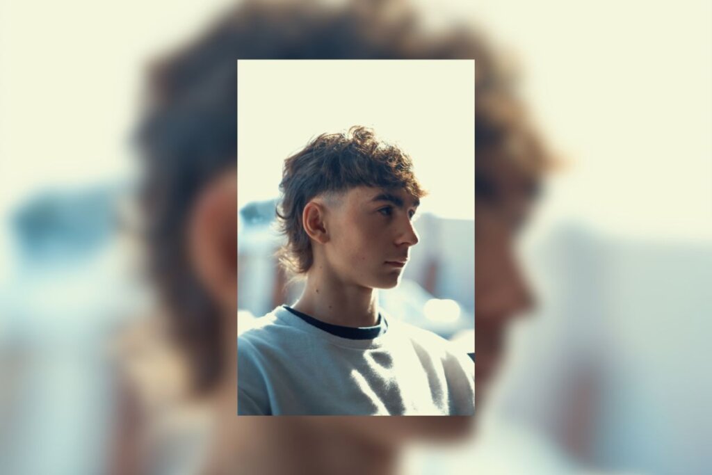 Menino com corte mullet moderno no cabelo, virado de lado e com o rosto iluminado pela luz do sol 