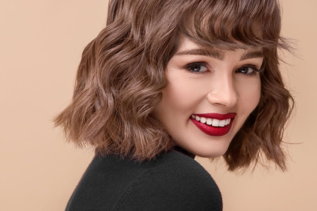 Mulher de batom vermelho e cabelo no tom mocha mousse sorrindo olhando para a câmera