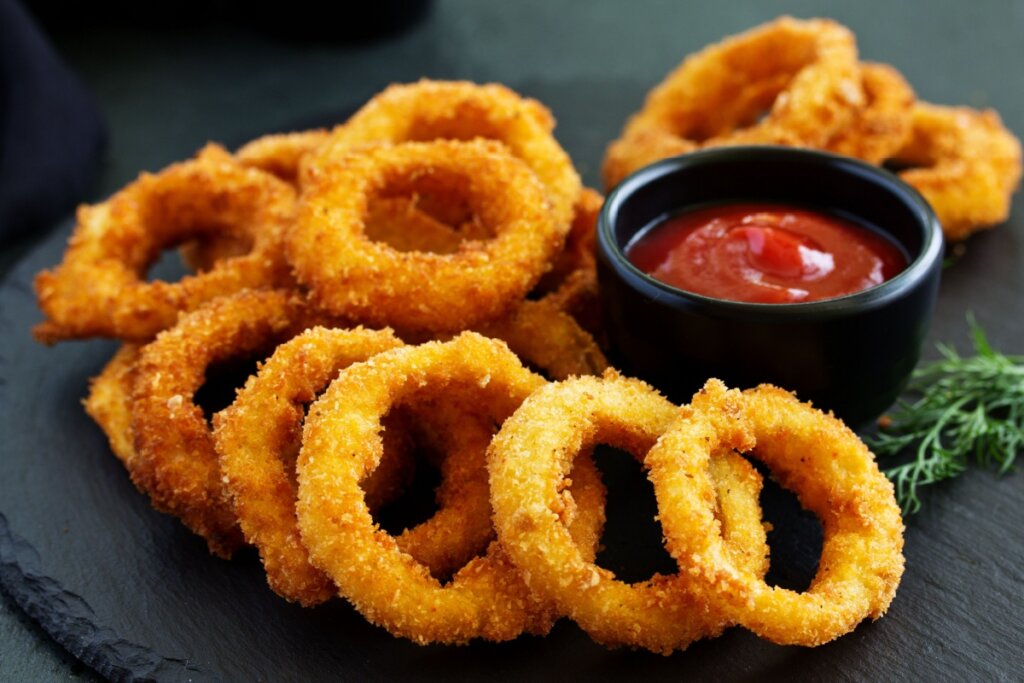 Anéis de cebola empanados ao lado de tigela de ketchup 