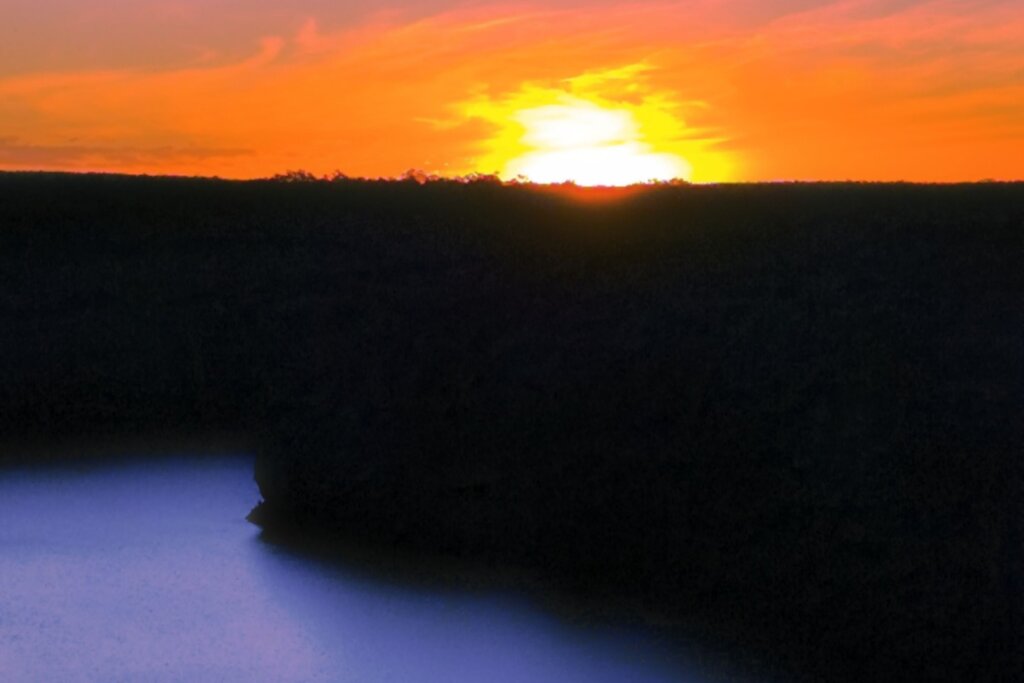 Pôr do sol no Cânion do Xingó com um rio e árvores abaixo dele 