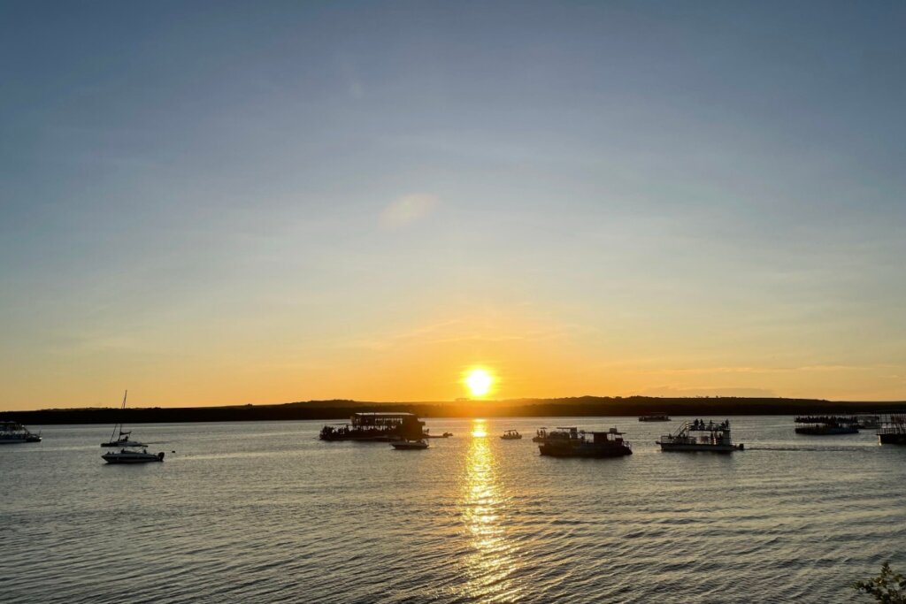 Pôr do sol sobre um rio com barcos e uma ilha ao fundo em João Pessoa 