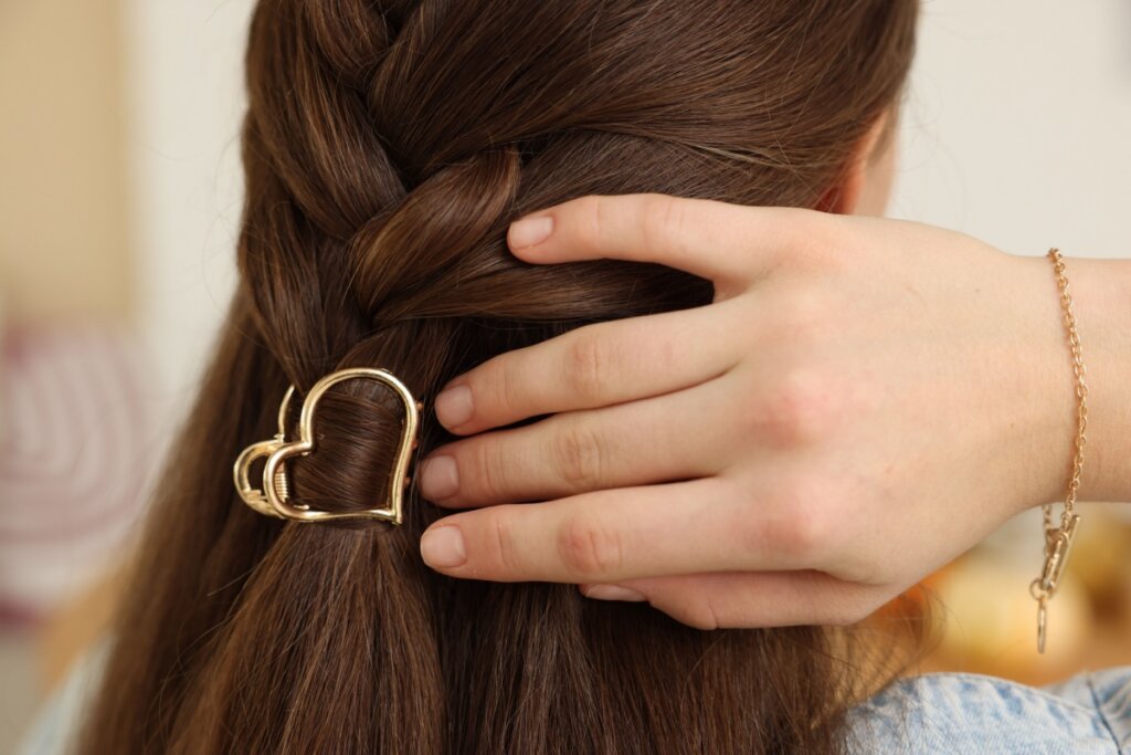 Presilha de metal dourada no formato de coração presa no cabelo castanho longo de uma mulher
