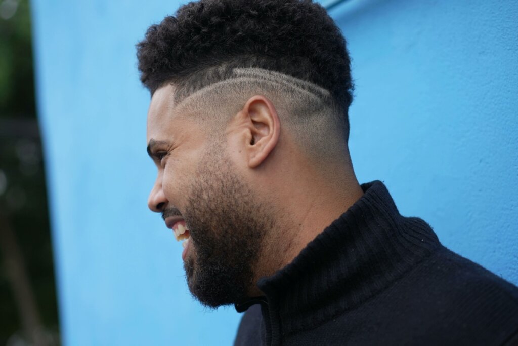 Homem sorrindo com o rosto virado de lado e cabelo afro fade