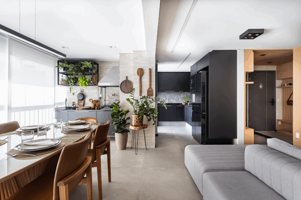 Sala de estar conectada com a de jantar em varanda, com decoração com elementos naturais em madeira e móveis em madeira e sofá cinza