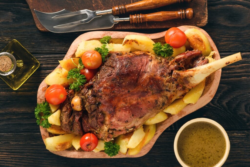 Paleta de cordeiro com batata e tomates-cereja, em cima de um recipiente de madeira, decorada com ramos de salsa