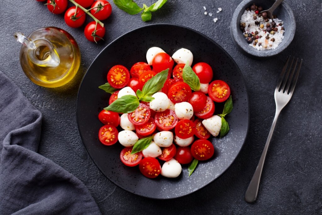 Prato preto com salada com tomates-cereja, muçarela de búfala e folhas de manjericão