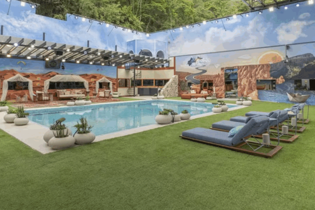 Área externa da casa do BBB 26 com piscina central, espreguiçadeiras, gramado e cenografia temática nas paredes