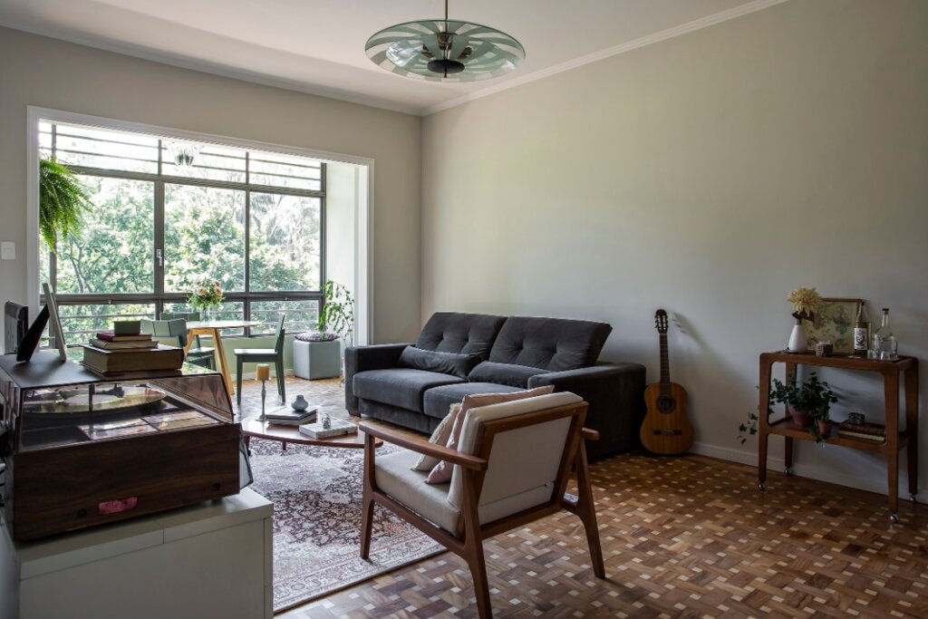 Sala de estar com sofá, poltrona, mesa lateral, instrumentos musicais e janela ao fundo