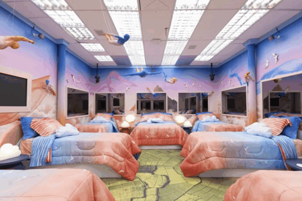 Quarto do BBB 26 com camas, roupas de cama em tons claros e elementos cenográficos no teto