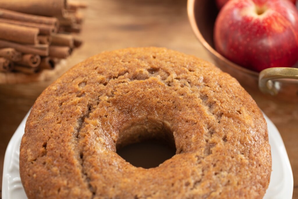 Bolo de maçã com canela servido em cima de mesa de madeira com maças e canela ao redor