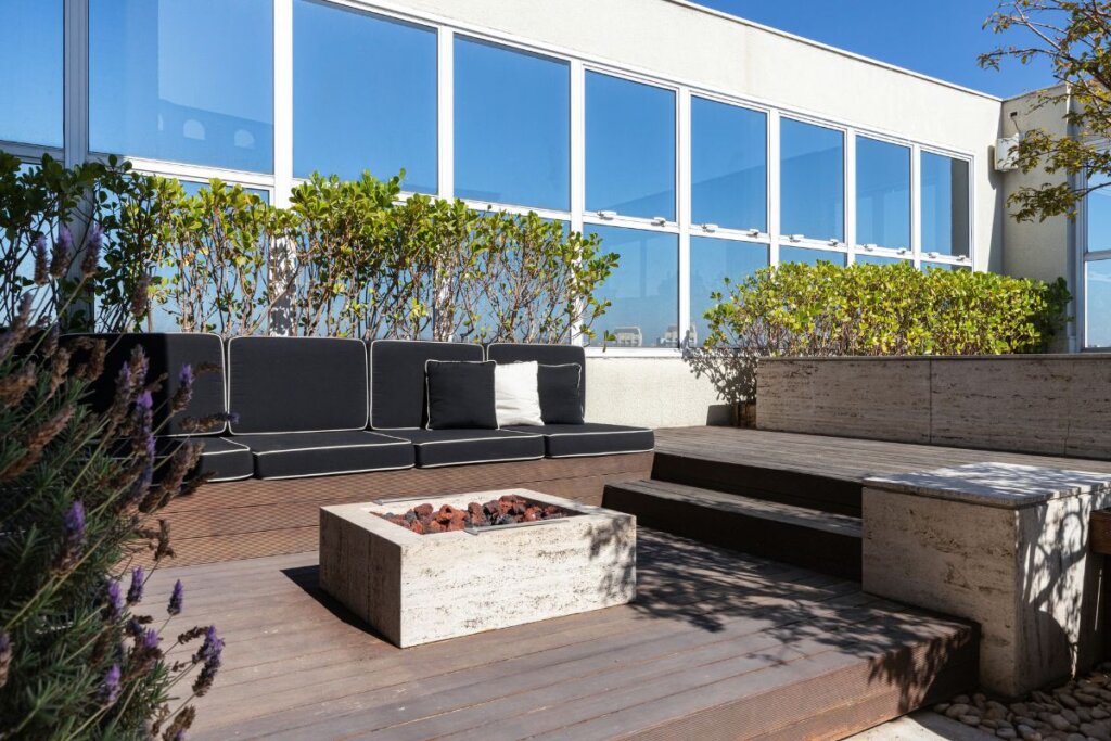 Jardim com deck de madeira, lareira com pedra natural e poltronas com estofado preto 